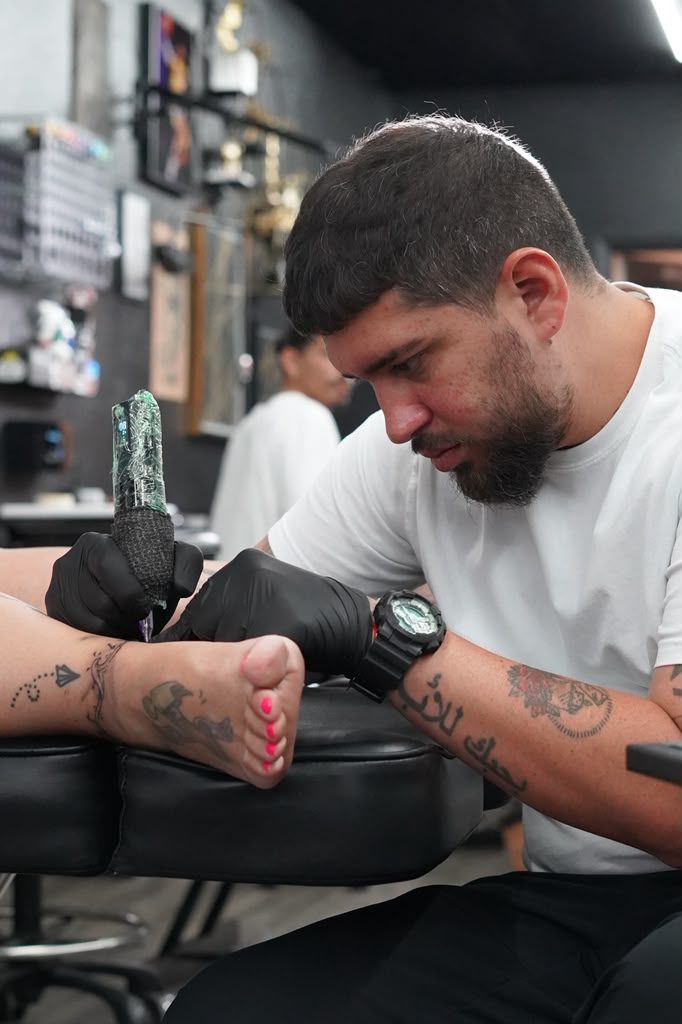 Roberto Ojeda tattooing a client's foot, head down, machine in hand
