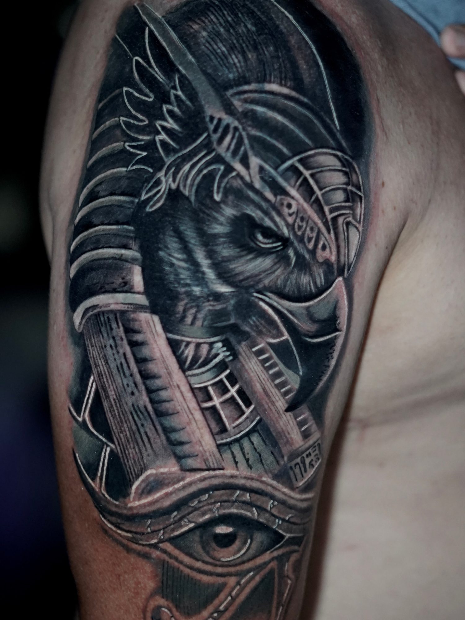Black and grey half sleeve tattoo of Horus with Egyptian columns and the Eye of Horus, on the upper arm