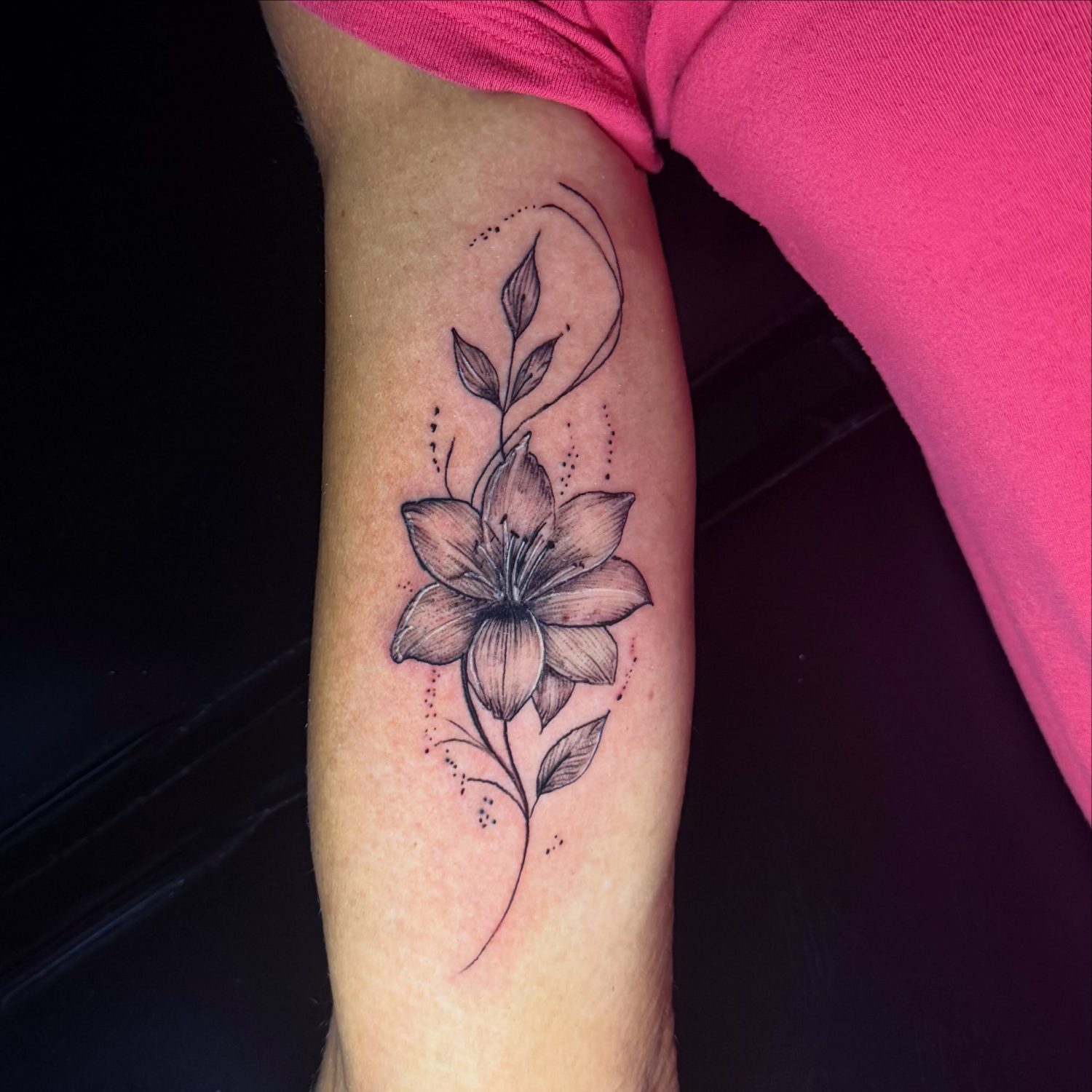 Fine line lily tattoo with leaves and dotwork on the upper arm